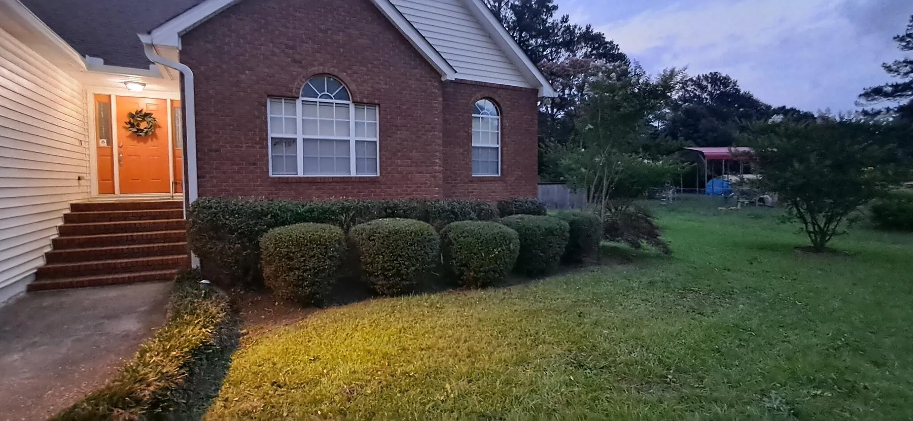 Front lawn cut and edged at a brick home with an orange door